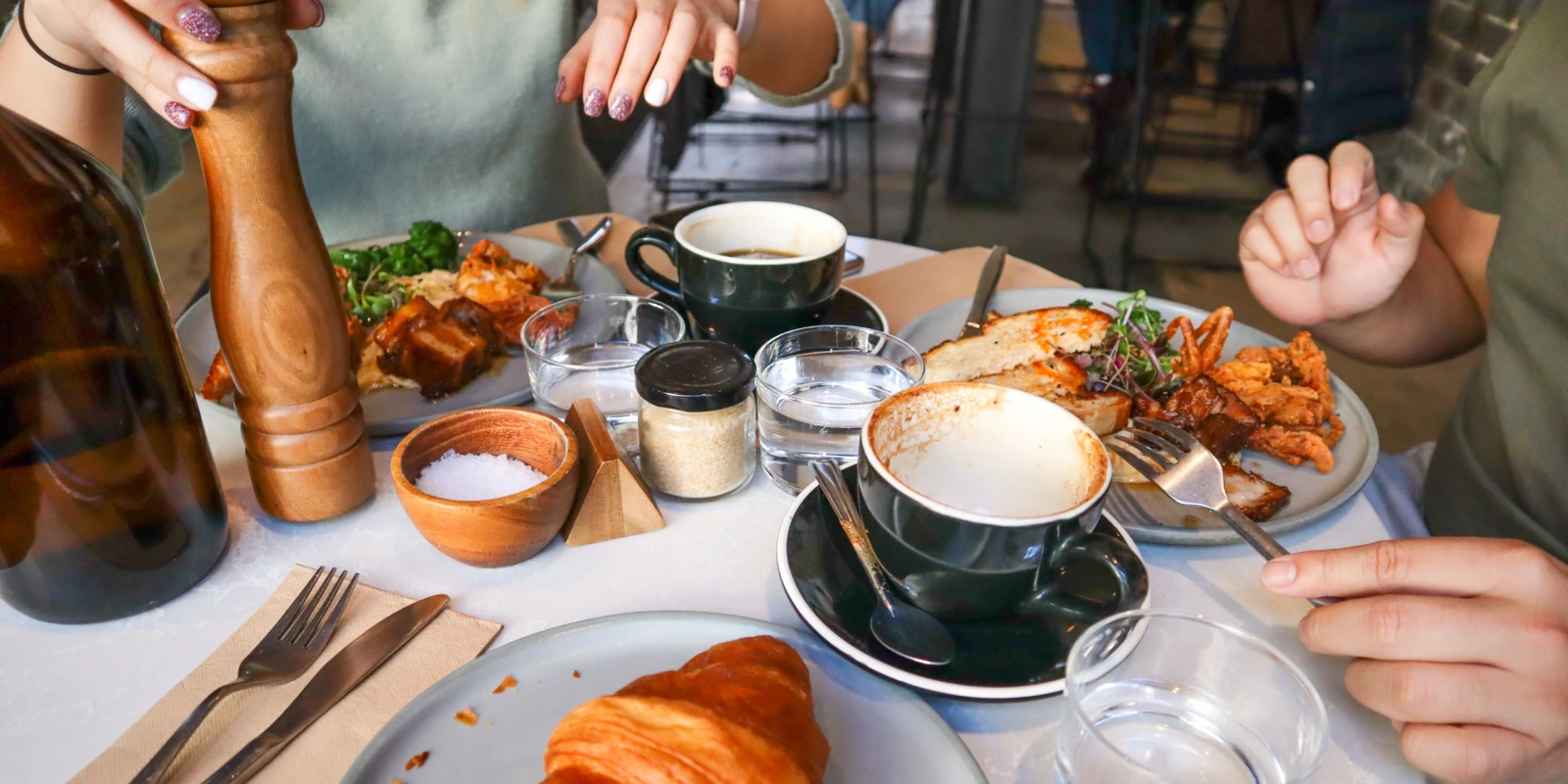 Mesa de brunch compartida con cafés, croissant, tostas y platos de huevos