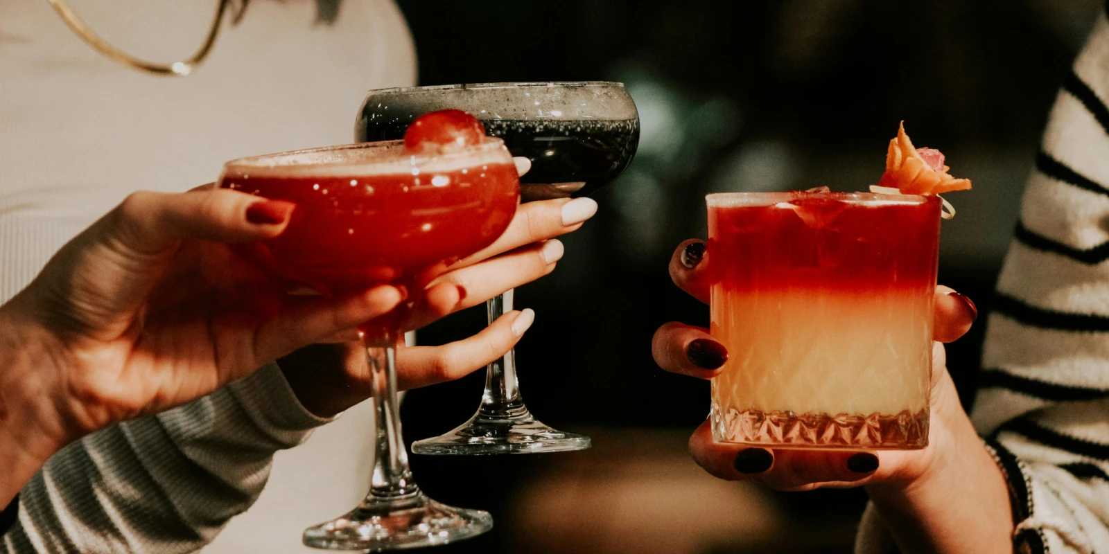Tres cócteles alzados para brindar, dos en copa y uno en vaso bajo con piel de naranja