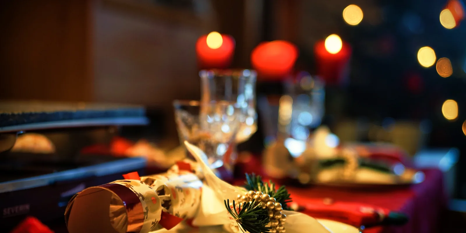 Mesa de restaurante puesta para Navidad, con copas, adornos y velas rojas desenfocadas al fondo