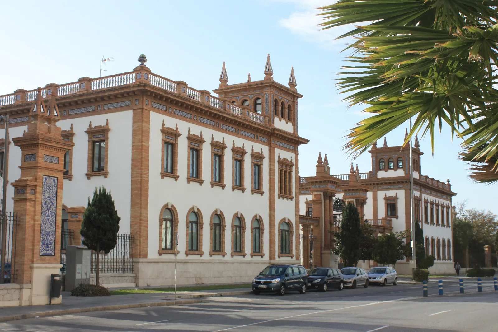 Pabellón neomudéjar de ladrillo y fachada blanca con torres de remate, junto a una avenida