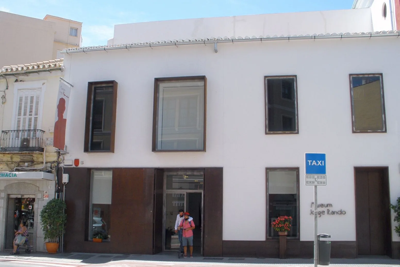 Fachada blanca con ventanales enmarcados en marrón y la puerta acristalada del museo