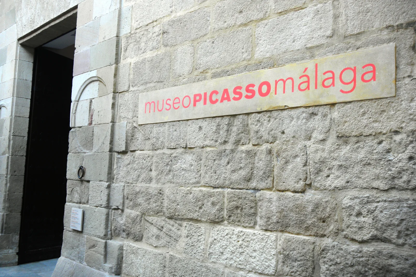 Puerta de piedra en un muro de sillería con el rótulo rojo del museo