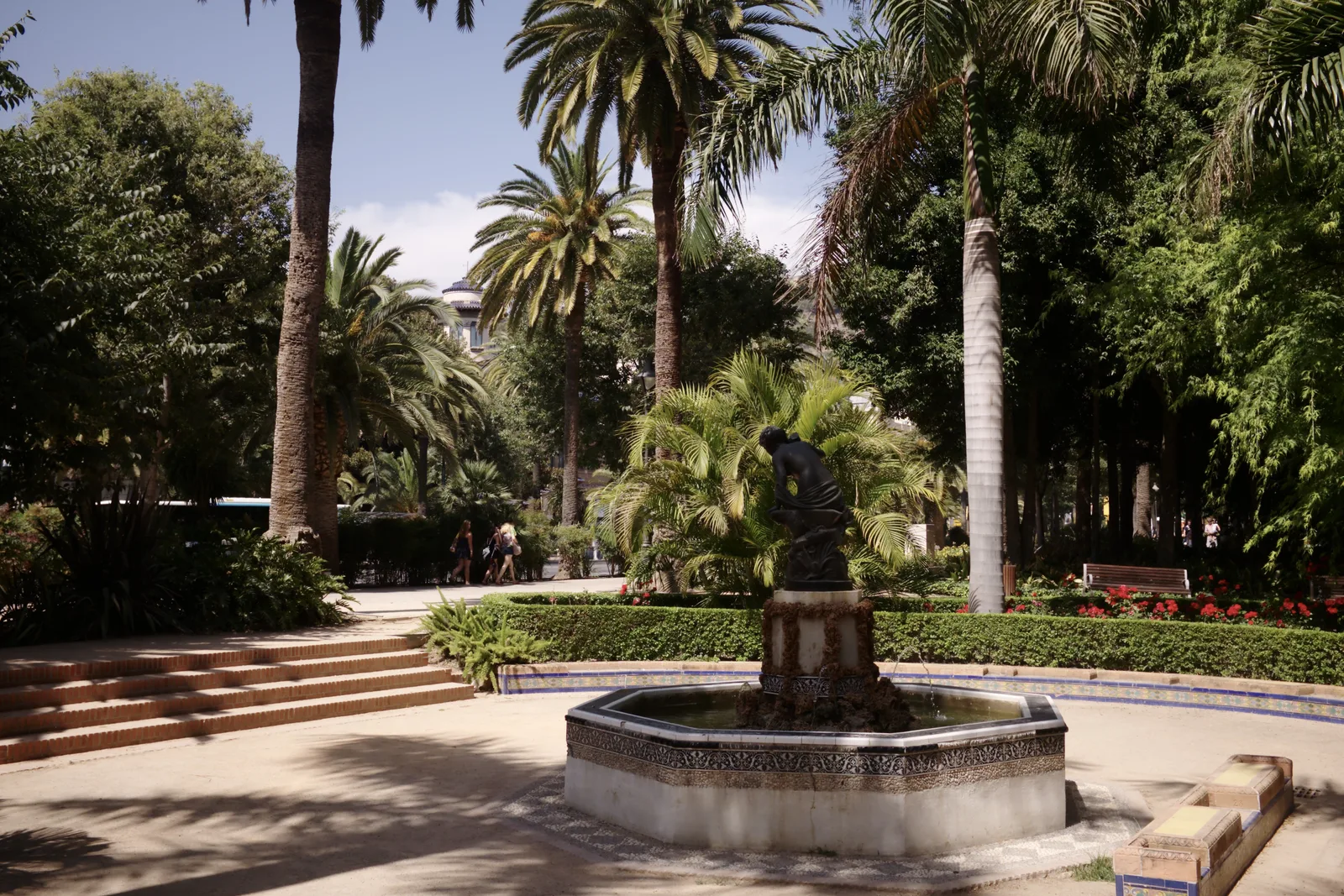 Fuente octogonal con una escultura en el centro, rodeada de palmeras y vegetación tropical