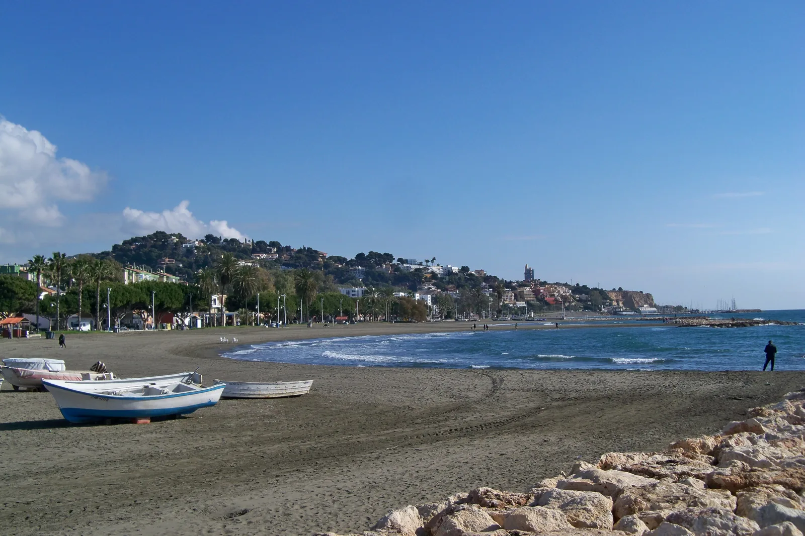 Playa de arena oscura con barcas de pesca varadas y casas en la ladera al fondo