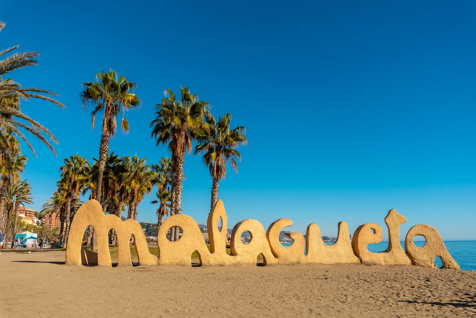 Letras gigantes de arena con el nombre de la playa entre palmeras, con el mar al fondo y cielo despejado